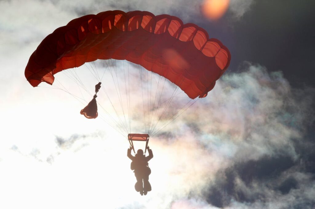 Silhouette of a parachuter descending against a vibrant sunset sky, capturing the thrill of aviation and freedom.