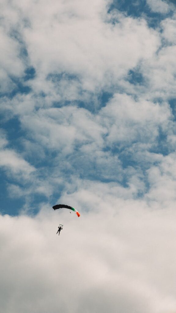 A skydiver descends with a parachute against a backdrop of cloudy sky, symbolizing freedom.