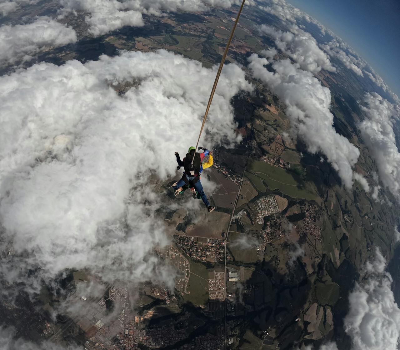 Tandem skydivers bravely descend through clouds with a parachute, capturing aerial views.