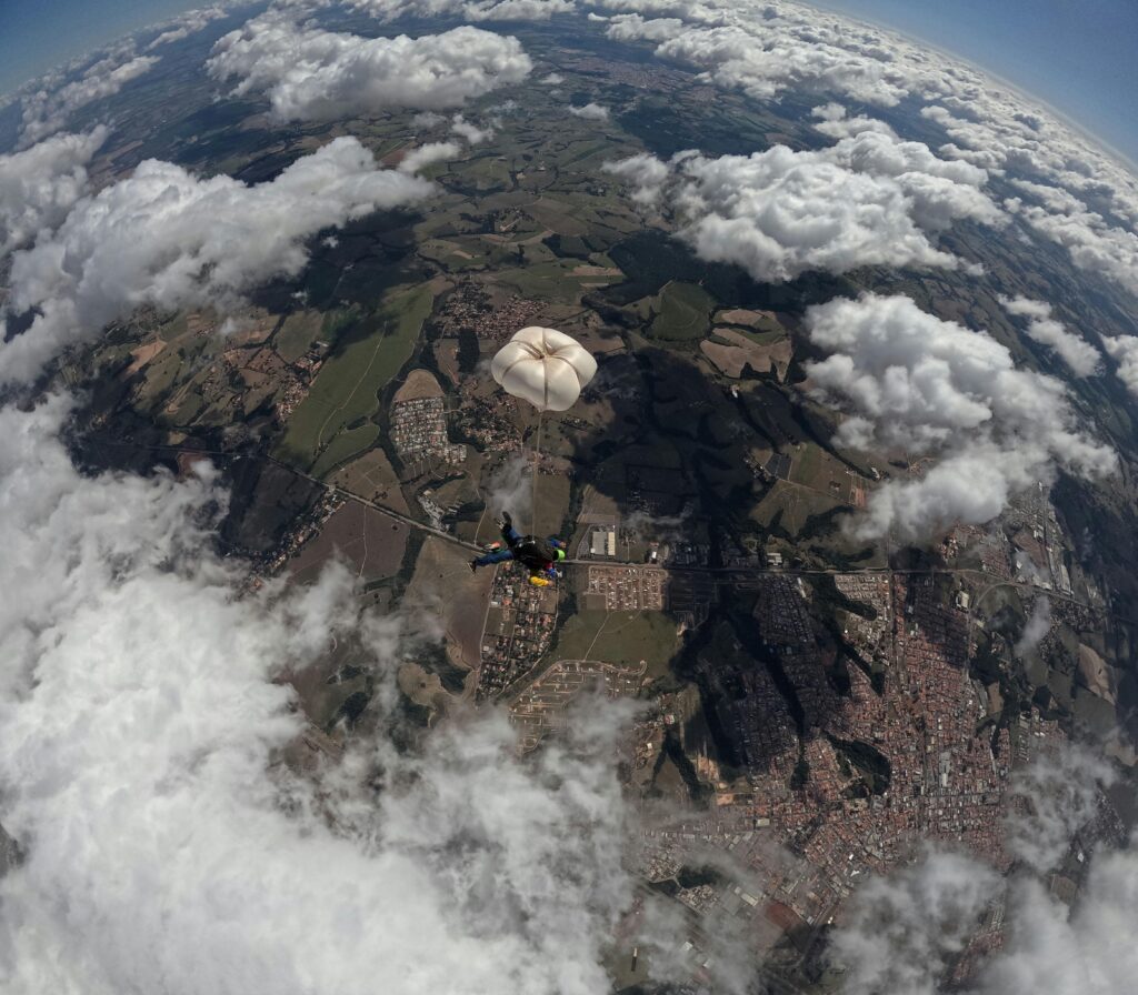 Aerial view of a skydiver with parachute above picturesque terrain and clouds.