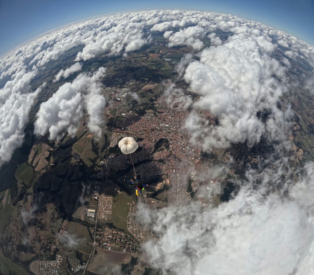Parachutist descends over cityscape with fluffy clouds and sprawling landscape below.