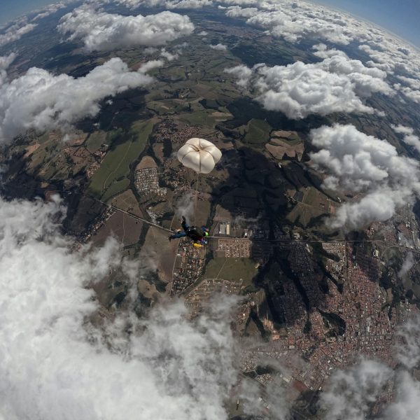 Aerial view of a skydiver with parachute above picturesque terrain and clouds.