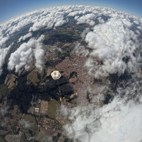 Parachutist descends over cityscape with fluffy clouds and sprawling landscape below.